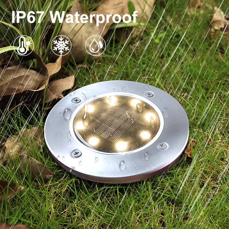 "Solar deck light with IP67 waterproof rating installed on green grass, illuminated during heavy rain."
